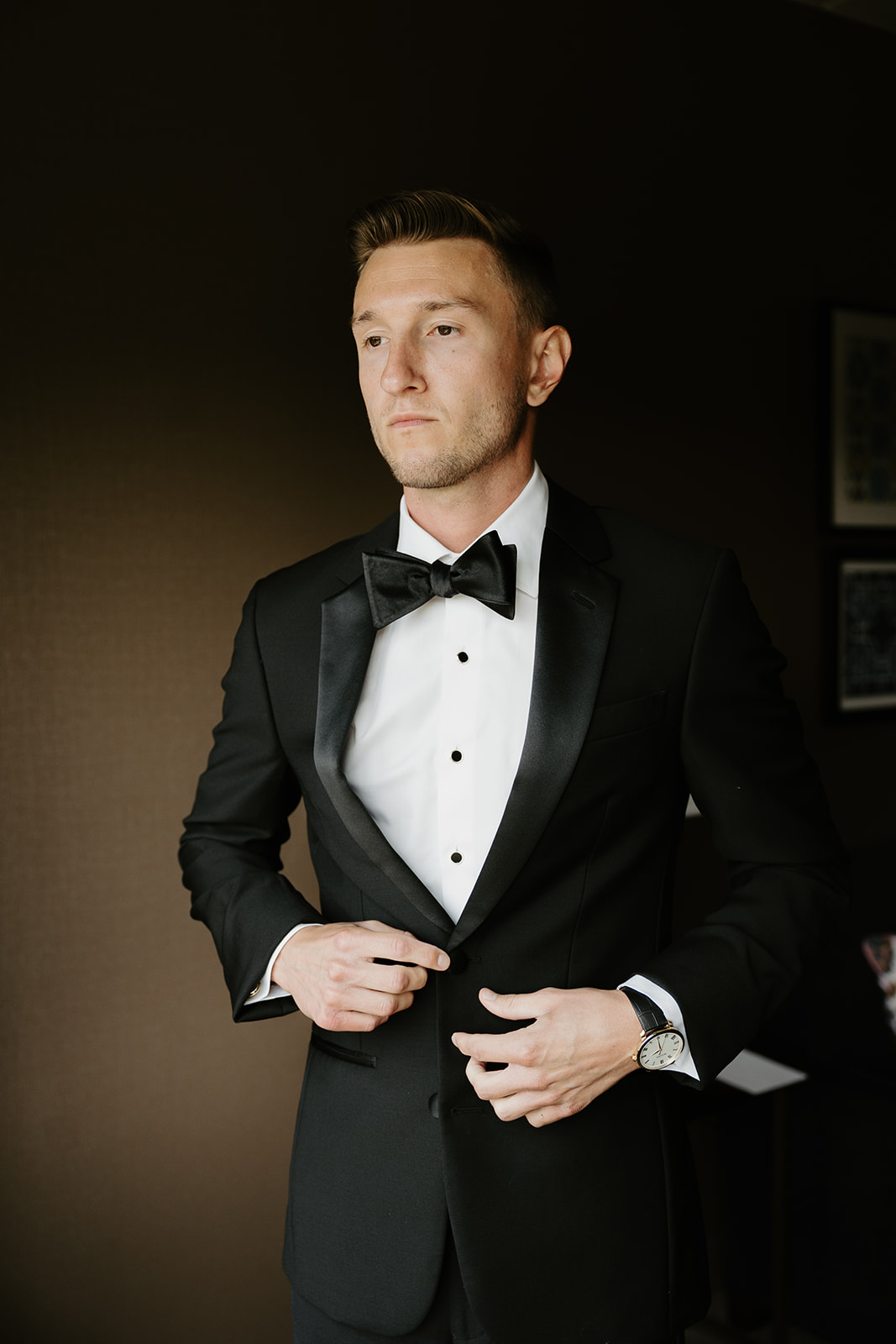Groom in a classic black tuxedo looking thoughtful while buttoning his jacket before the ceremony.